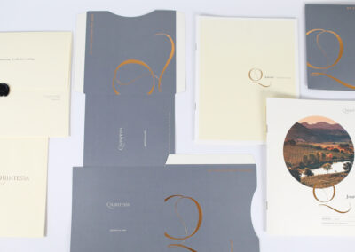 A photo with a collage of printed marketing collateral produced by Qualprint with gold foil accents and embossing for Quintessa, a wine premier wine brand.